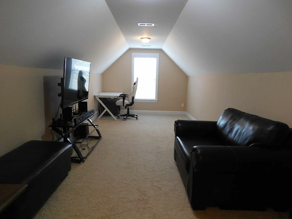 A black couch sits in a room with a television and a desk.