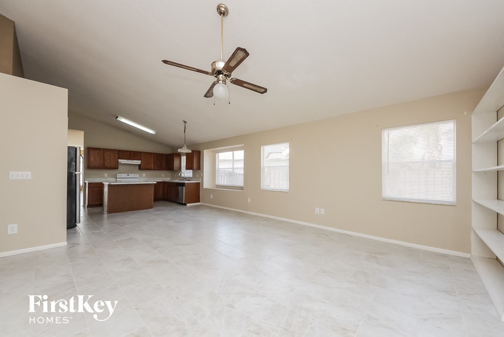 an empty living room with a ceiling fan and a kitchen