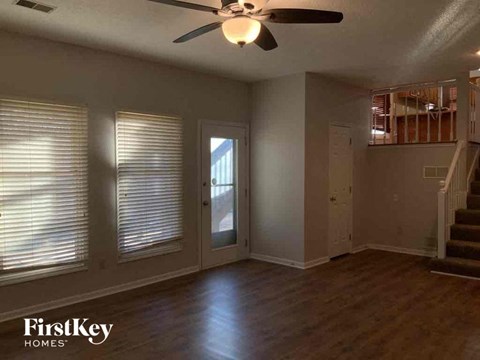 an empty living room with a ceiling fan and a door to a staircase