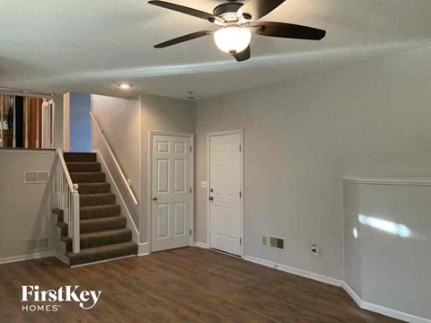 an empty living room with a ceiling fan and stairs