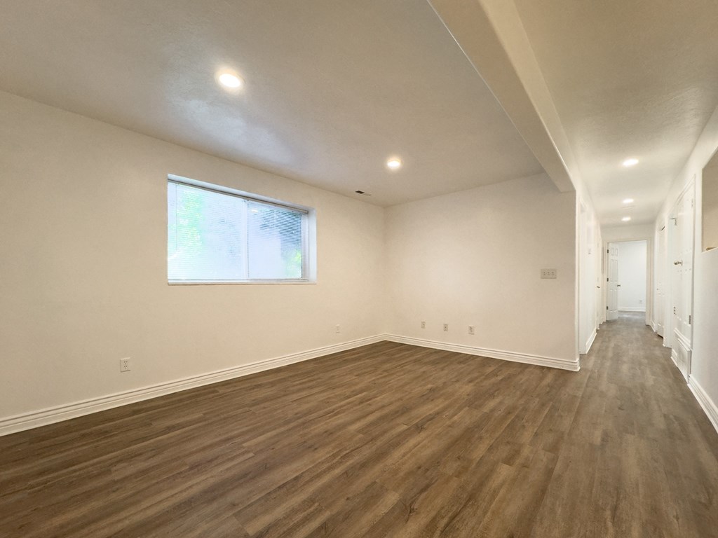 a living room with white walls and wooden floors and a window