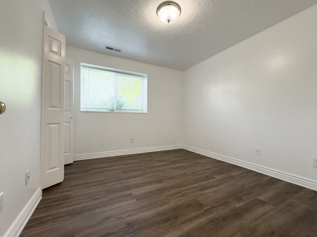 an empty living room with wood flooring and a window