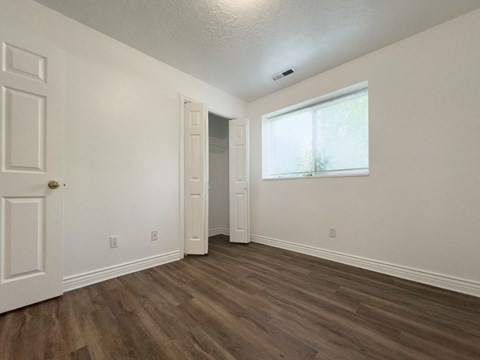a bedroom with white walls and wood flooring and a window