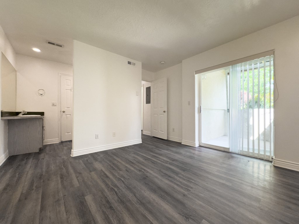 an empty living room with a sliding glass door to a kitchen