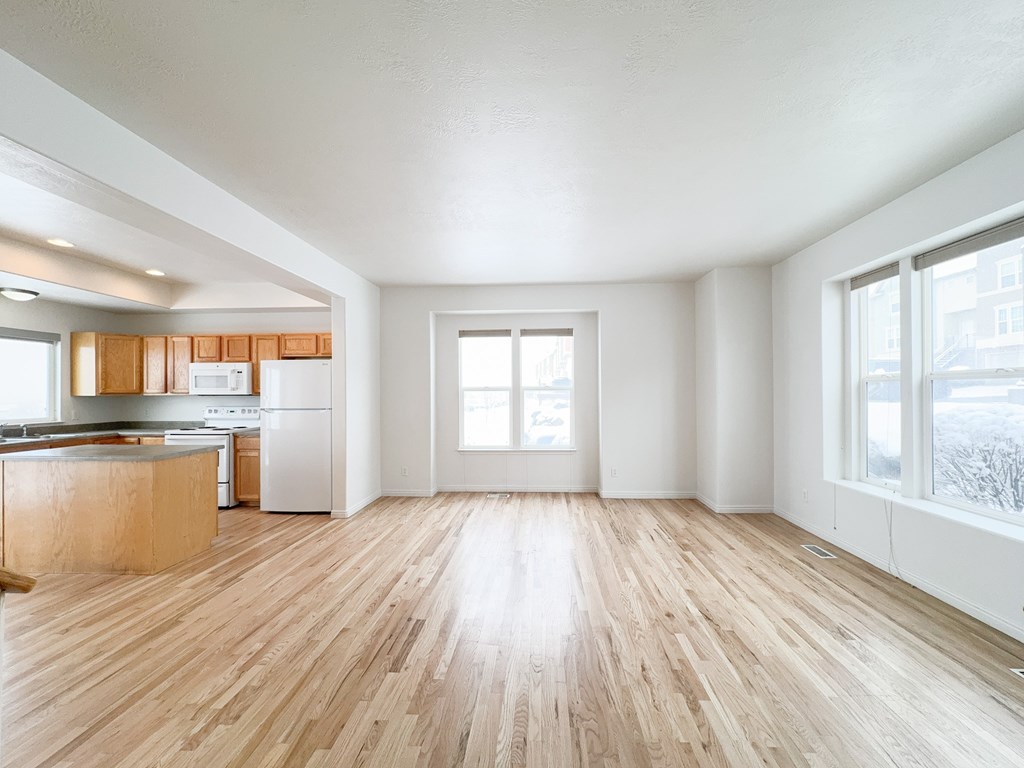 an empty living room with wood floors and a kitchen