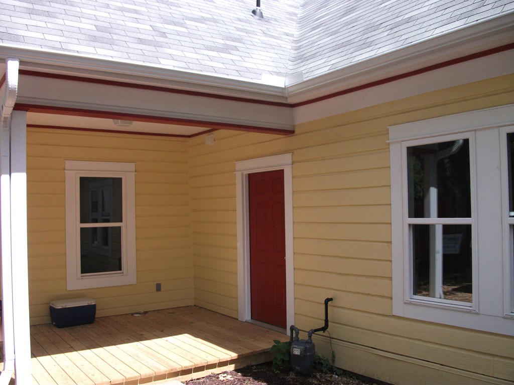a yellow house with a deck and a red door