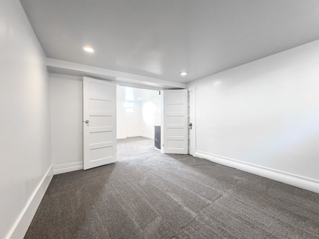 a living room with white walls and carpet and a door to a closet