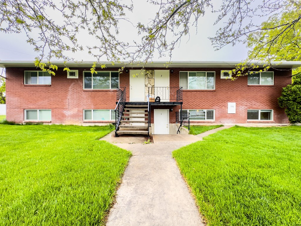 front view of a brick apartment building with a walkway and grass