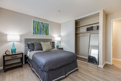 A bedroom with a bed, nightstand, and a painting on the wall.