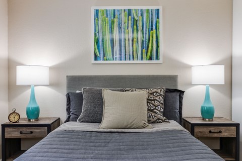 A bedroom with a bed, two lamps, and a painting on the wall.