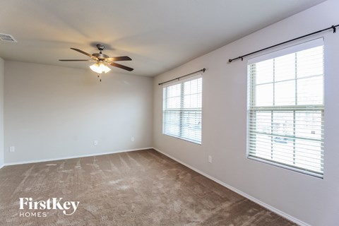 A spacious room with a ceiling fan and two windows with blinds.
