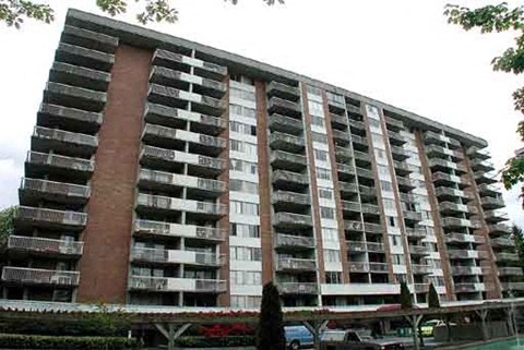 A large apartment building with balconies and a parking lot in front.