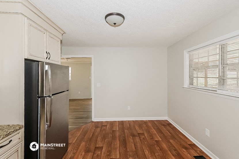 an empty kitchen with a stainless steel refrigerator and wooden floors