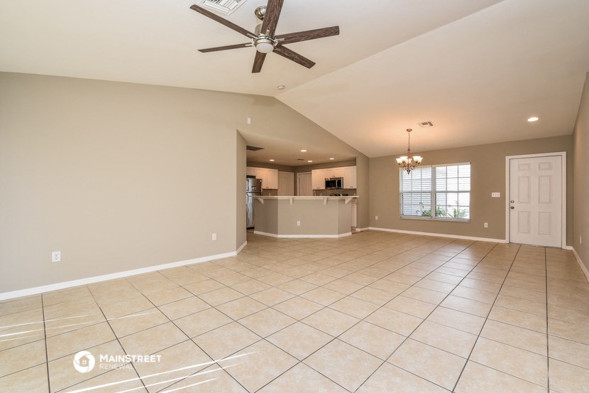 an empty living room with a kitchen in the background
