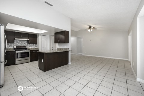 an open kitchen and living room with white tile flooring and black cabinets