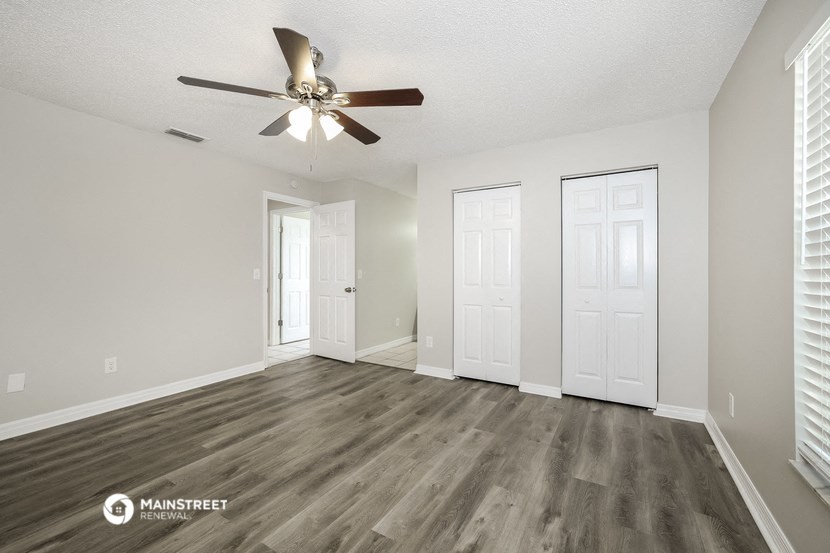 the spacious living room with white walls and a ceiling fan