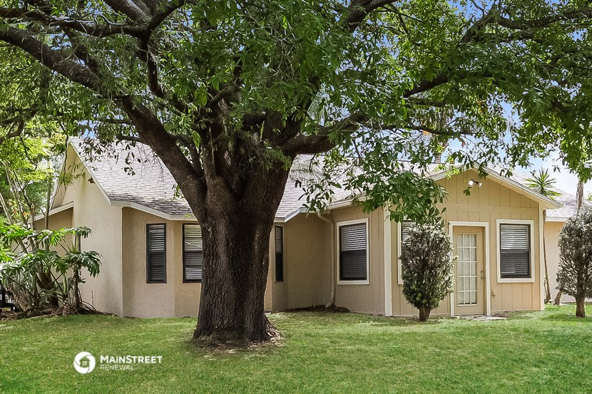 a small yellow house with a large tree in the yard