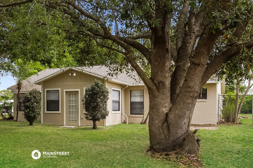 a small tan house with a large tree in the yard