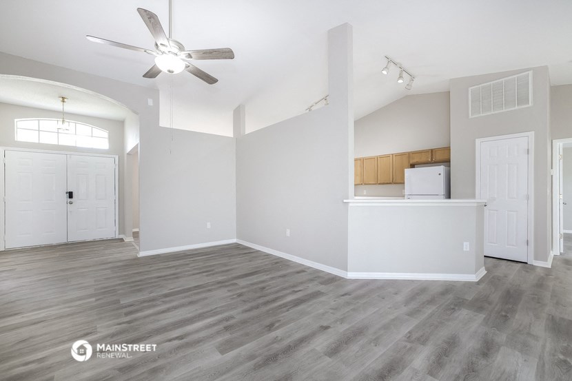 an empty living room with a ceiling fan and a kitchen