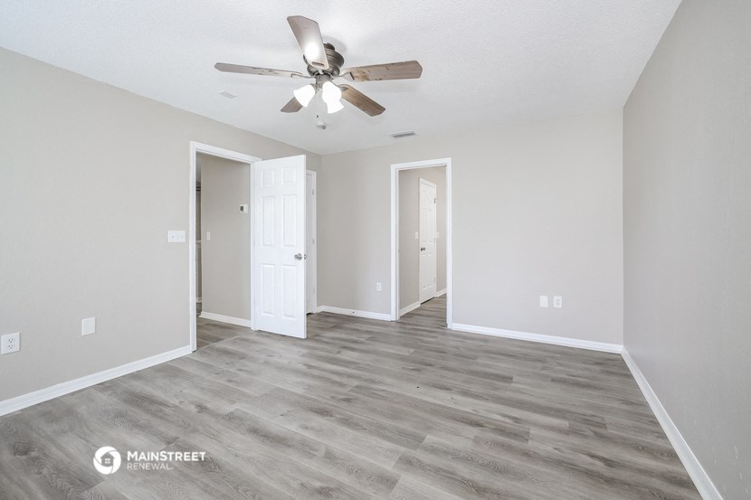 the spacious living room with a ceiling fan and white walls