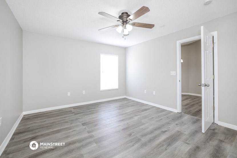 the spacious living room with a ceiling fan and white walls