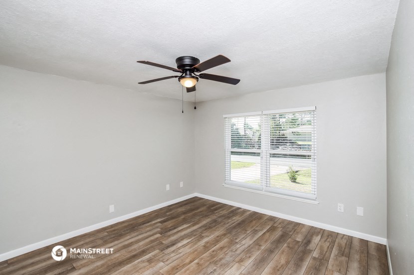 the spacious living room with a large window and a ceiling fan