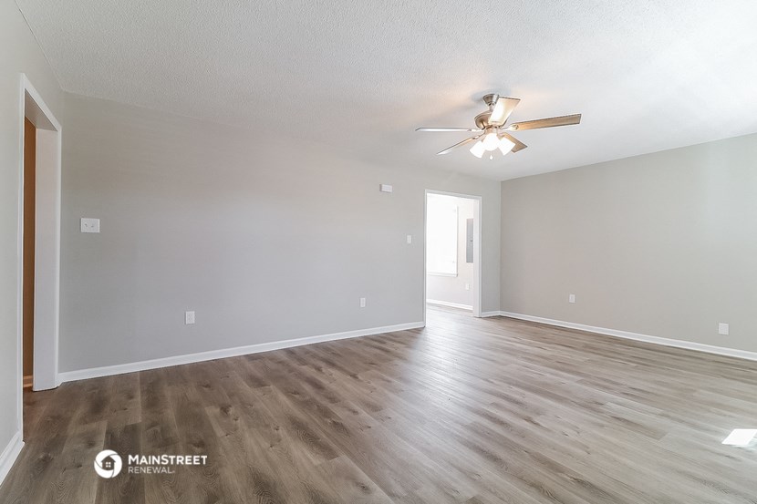 the spacious living room with wood flooring and a ceiling fan