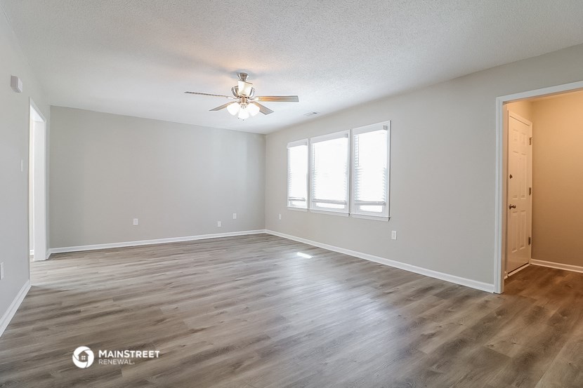 the spacious living room with hardwood flooring and a ceiling fan