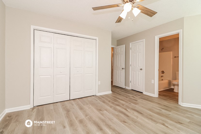 the spacious living room with a ceiling fan and doors to the bathroom