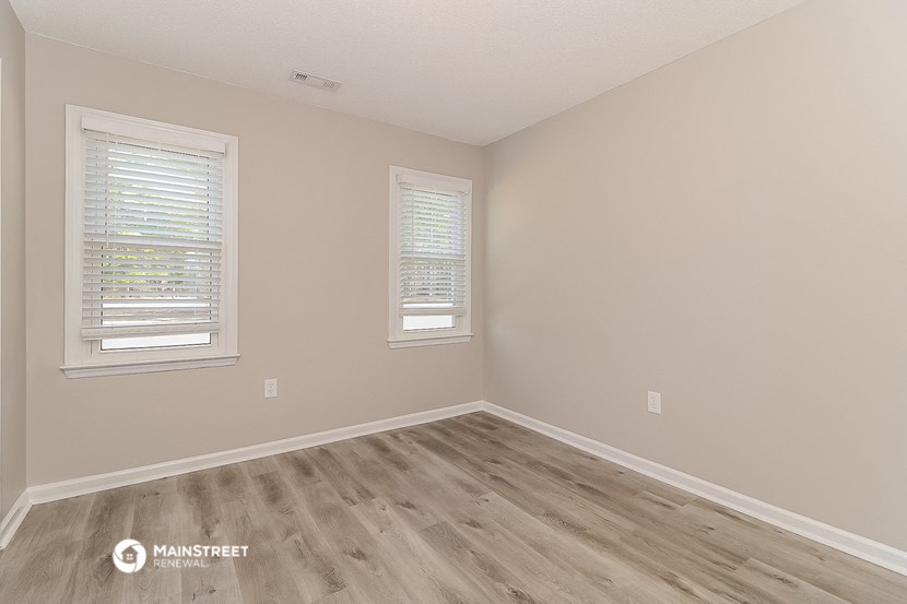the spacious bedroom with hardwood flooring and two windows