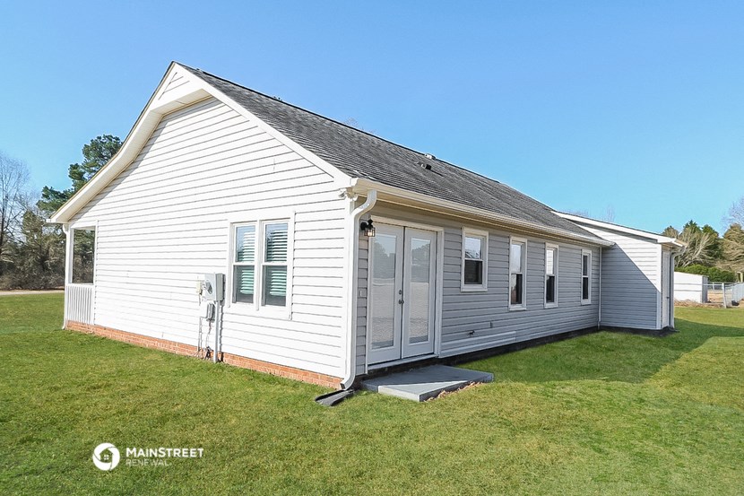 the front of a small white house with a porch and a lawn