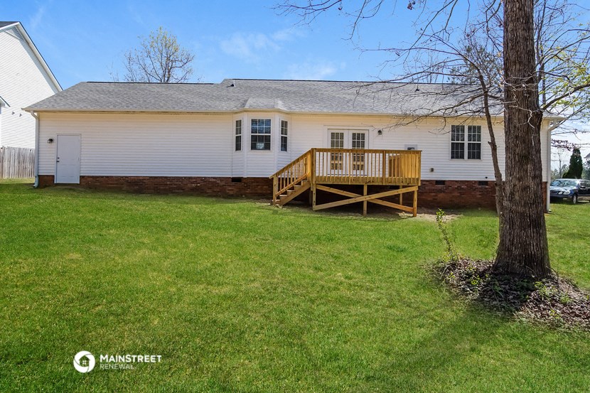 the back of a white house with a deck and a tree