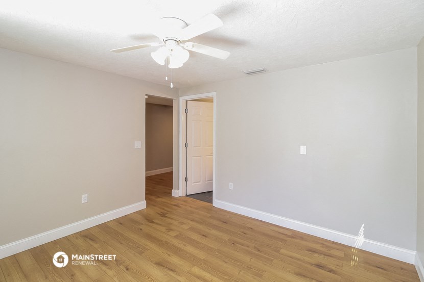the spacious living room with hardwood flooring and a ceiling fan