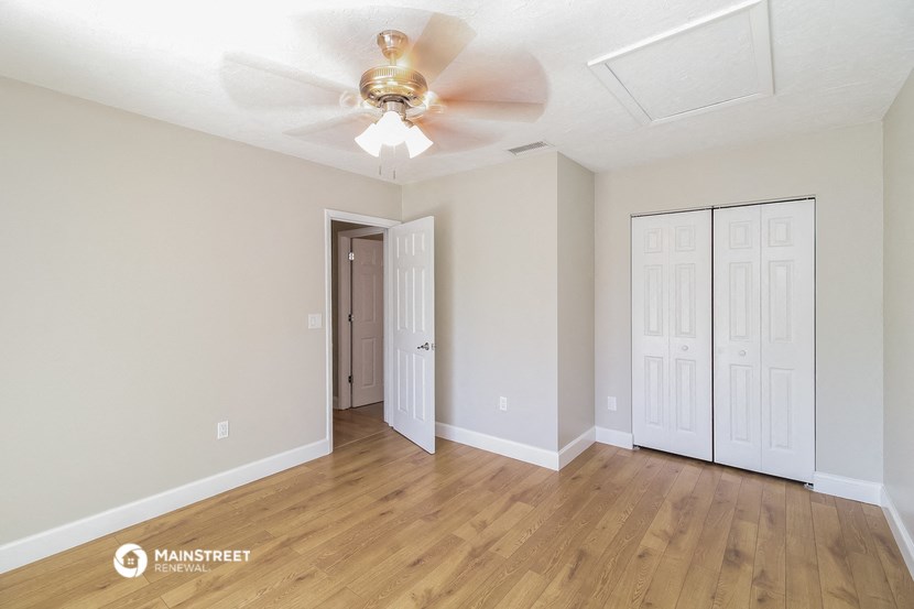 the spacious living room with white walls and a ceiling fan