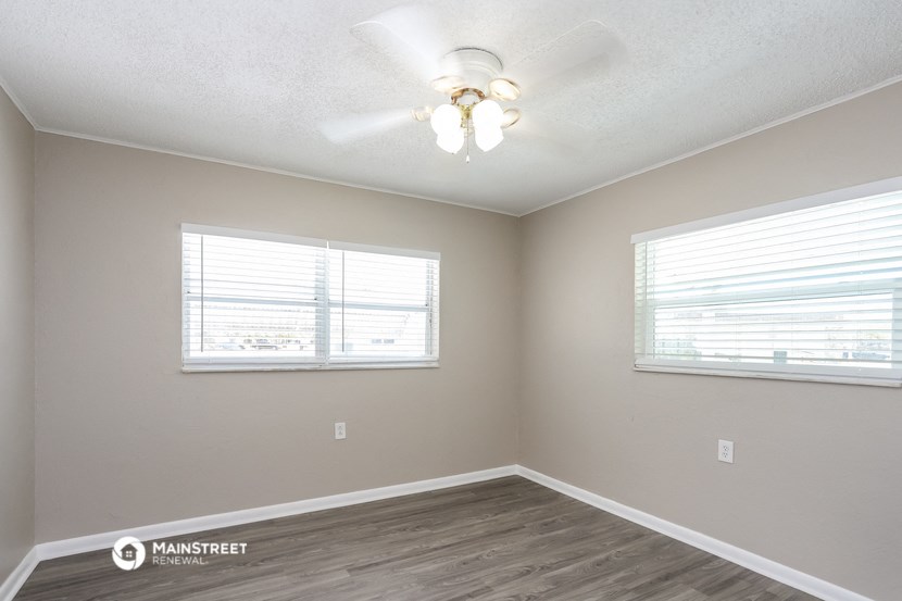 an empty bedroom with a ceiling fan and two windows