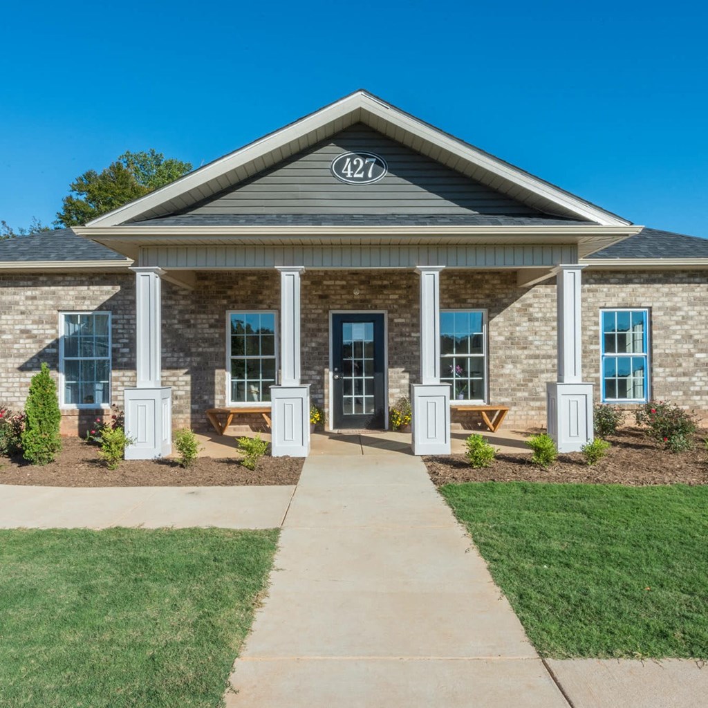 the front of a brick house with white pillars and a sidewalk