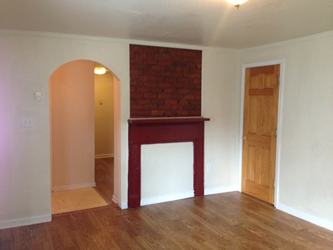 an empty living room with a fireplace and wooden floors