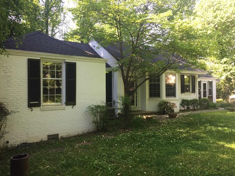 A white house with black shutters and a tree in front.