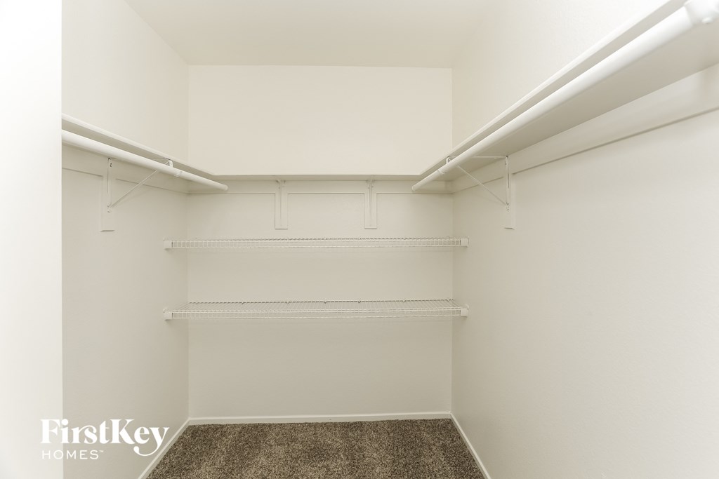 a spacious walk in closet with white walls and white shelves