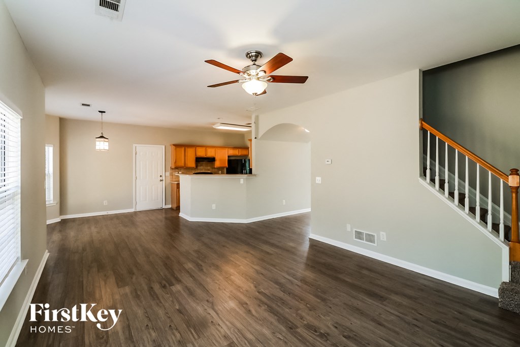 an empty living room with a ceiling fan and a staircase