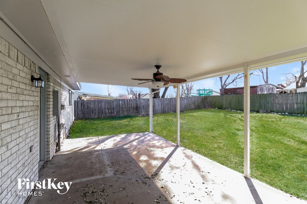 the covered patio in the backyard of a home with a ceiling fan
