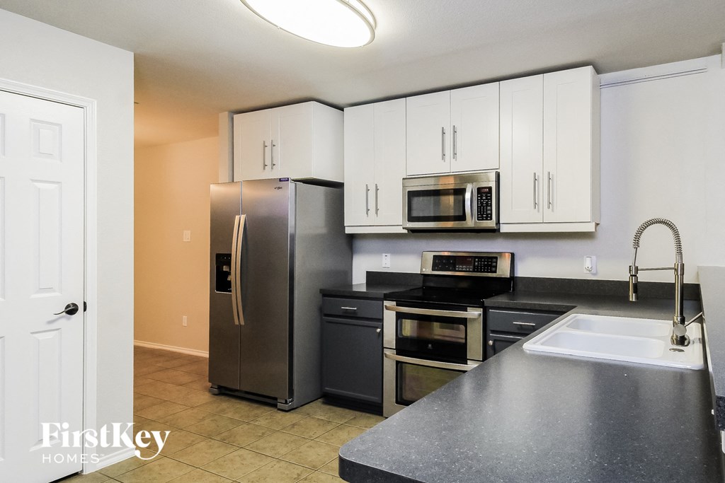 A kitchen with a refrigerator, microwave, oven, and sink.