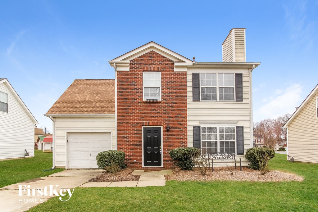 two story brick home with black door and white garage doors on a green lawn