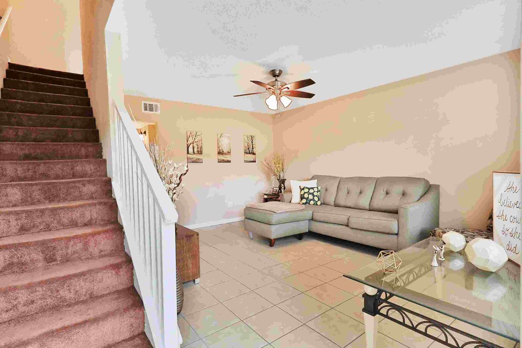 a living room with couches and a glass table    and a staircase