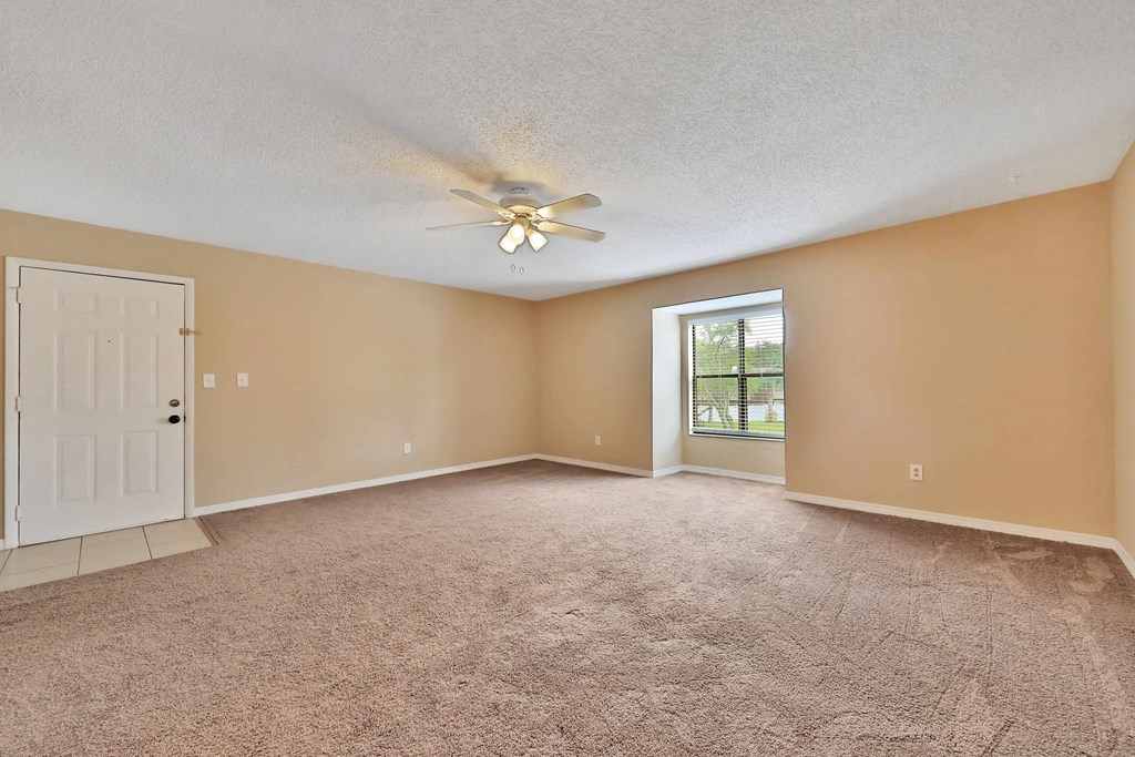 an empty living room with a white door and a ceiling fan