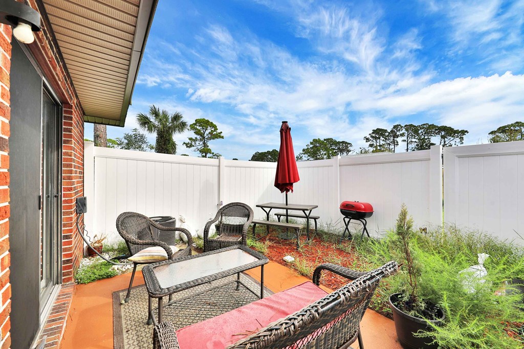 a patio with a white fence and chairs and an umbrella