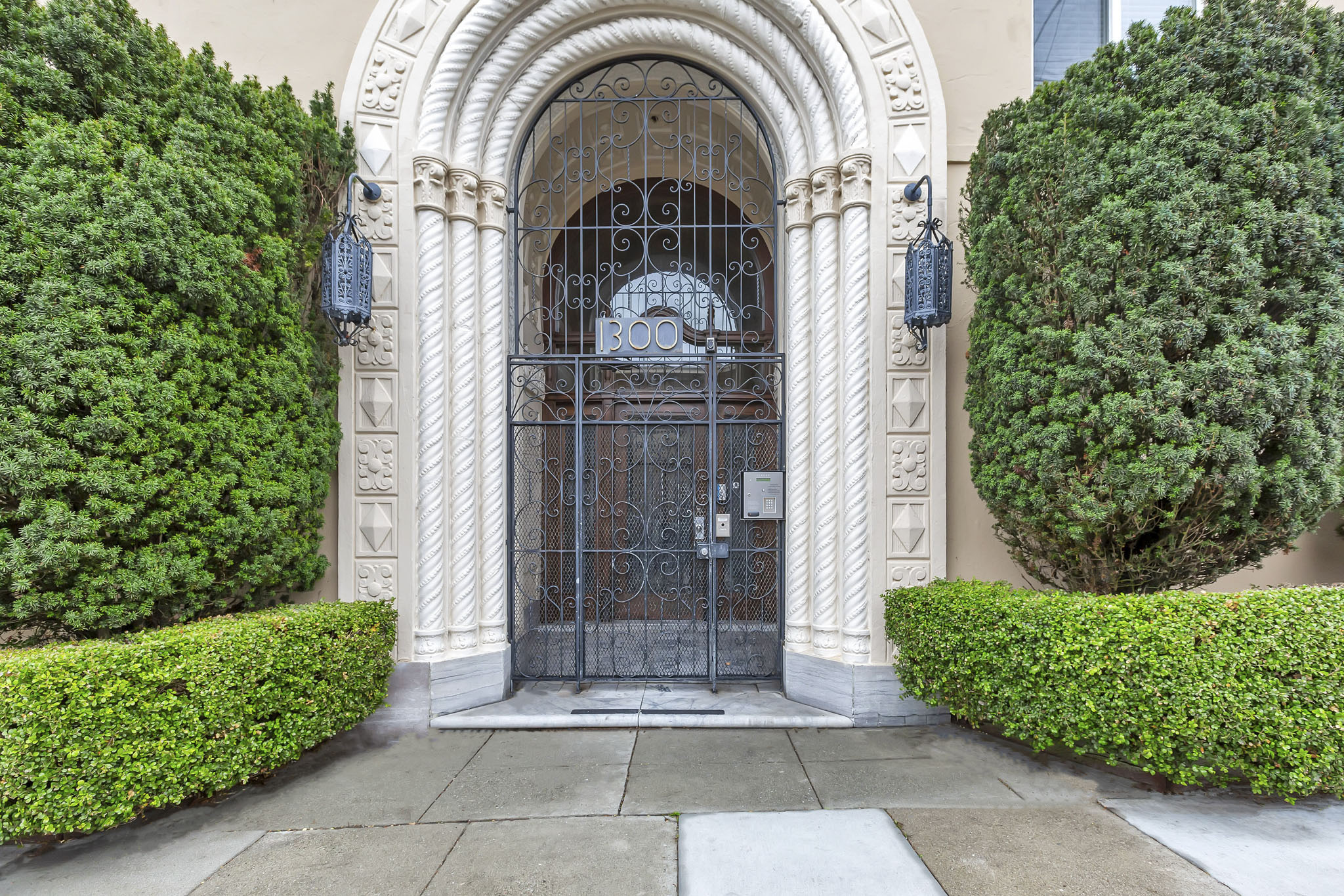 A large, ornate gate is the centerpiece of a well-manicured entrance.