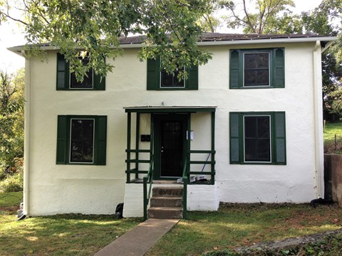 A white house with green shutters and a green door.