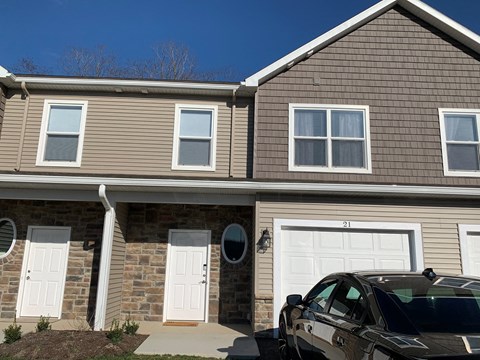 a brown house with white doors and a black car parked in front
