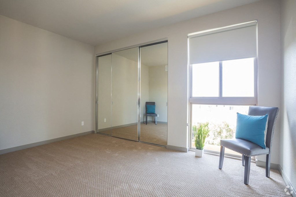 a living room with a chair and a window and a mirrored closet